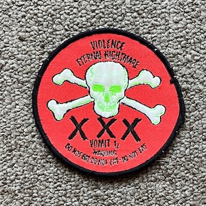 Op de afbeelding: Een ronde patch met een rode achtergrond en een zwarte rand. De patch toont een groene schedel met gekruiste botten, en de tekst "VIOLENCE ETERNAL NIGHTMARE" en "VOMIT 12 WARNING DO NOT EAT".