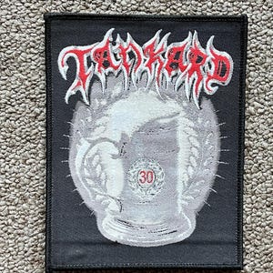 May include: Black rectangular patch featuring the band name "Tankard" in red and white, stylized lettering. The patch design includes a white beer stein with a "30" in the center, surrounded by a wreath.