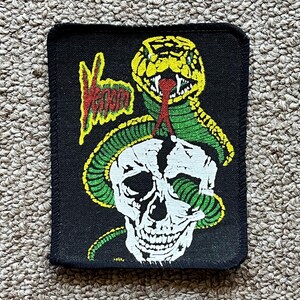 May include: Black patch featuring a white skull with a green and yellow snake wrapped around it. The word "Venom" is written in yellow and red. The patch has a black border.