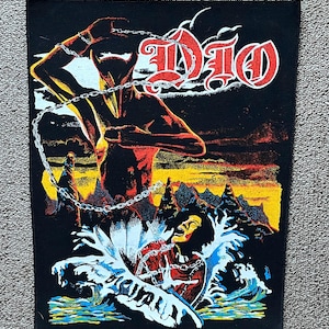 Op de afbeelding: Zwarte patch met een rood en wit "DIO" logo. De afbeelding toont een gehoornde figuur met kettingen tegen een vurige zonsondergang. Een figuur is ondergedompeld in water.
