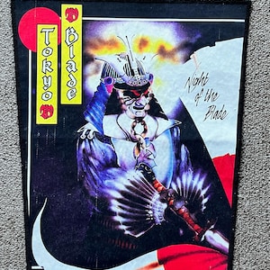 Puede incluir: Un parche en blanco y negro con un guerrero samurái sosteniendo una espada. El guerrero lleva un casco y una armadura. El parche tiene el texto "Tokyo Blade" y "Night of the Blade".