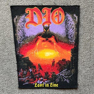 May include: Black patch featuring the band name "DIO" in orange gothic lettering above a fiery scene. The image depicts a horned figure in front of a sunset, with the text "Last in Line" below.