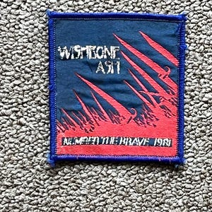 May include: A square patch with a blue background and red and white graphics. The text "WISHBONE ASH" is at the top, with "NUMBERED THE BRAVE 1981" at the bottom. The patch has a blue border.
