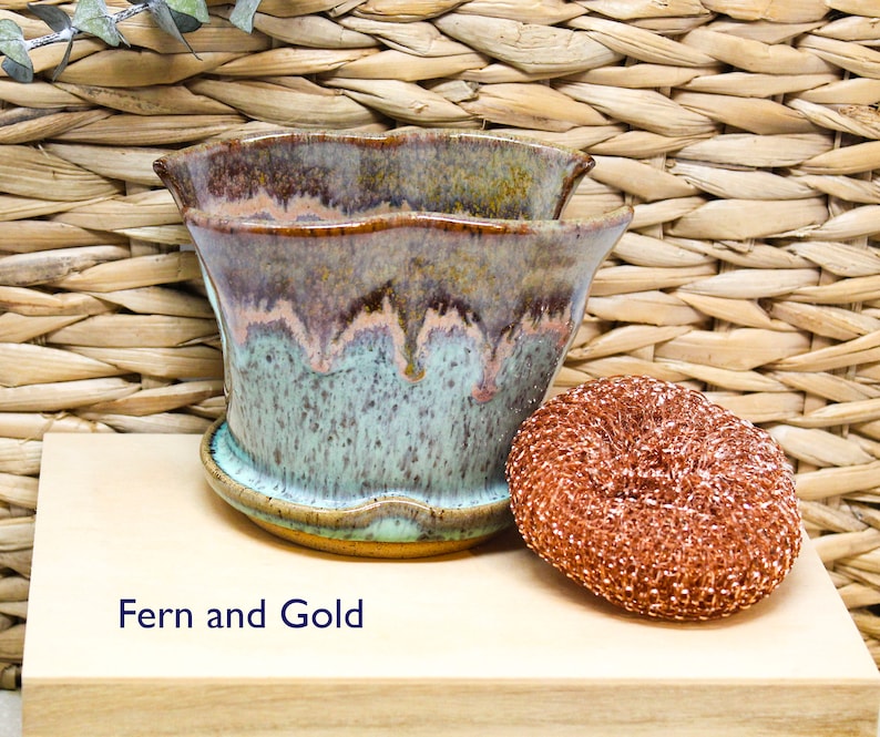 May include: A ceramic planter with a wavy rim, featuring a green, brown, and pink glaze. The planter is labeled "Fern and Gold".