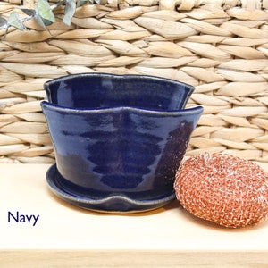 May include: A navy blue ceramic planter with a wavy rim and a matching saucer. The planter is sitting on a light wood surface.