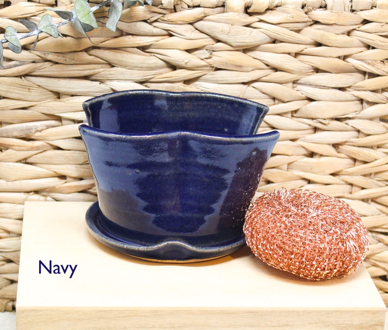 May include: A navy blue ceramic planter with a wavy rim and a matching saucer. The planter is sitting on a light wood surface.
