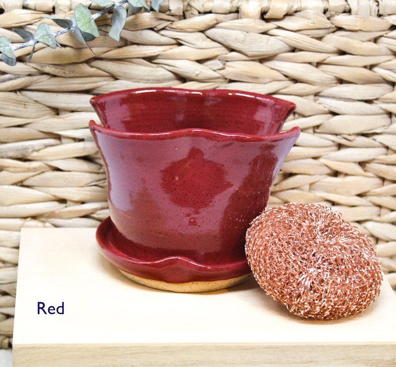May include: Red ceramic planter with a scalloped rim and a matching saucer. The planter is sitting on a light wood surface.