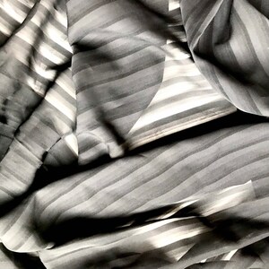 May include: Black and white striped fabric with a smooth, silky texture. The fabric is folded and draped, creating a soft, flowing look.