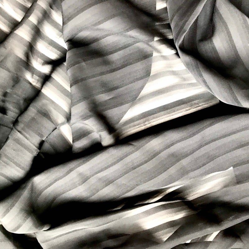 May include: Black and white striped fabric with a smooth, silky texture. The fabric is folded and draped, creating a soft, flowing look.