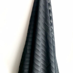 May include: Black fabric with a subtle striped pattern. The fabric is draped over a white surface.