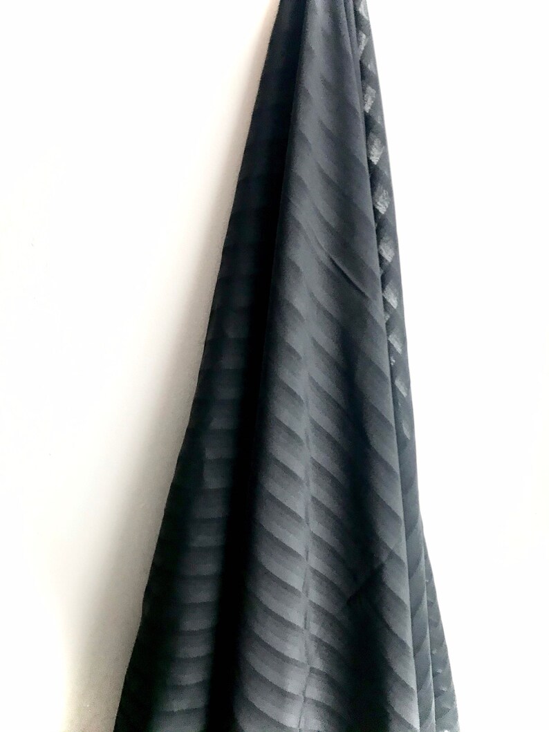 May include: Black fabric with a subtle striped pattern. The fabric is draped over a white surface.