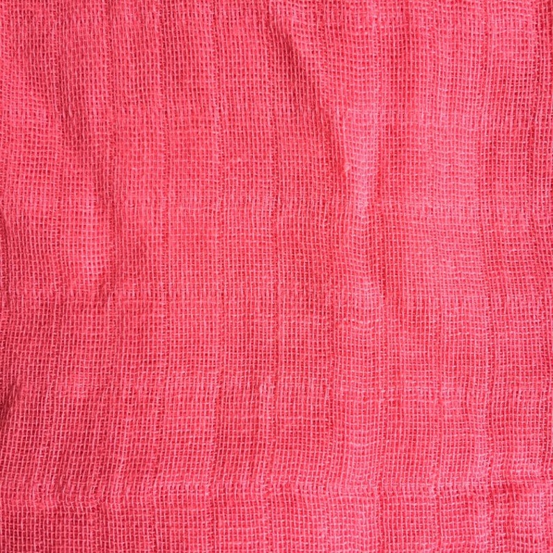 May include: A close-up of a pink fabric with a woven texture. The fabric has a slightly wrinkled appearance.