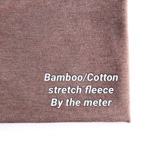 May include: Close-up of a brown stretch fleece fabric with the text "Bamboo/Cotton stretch fleece By the metre" printed on it.