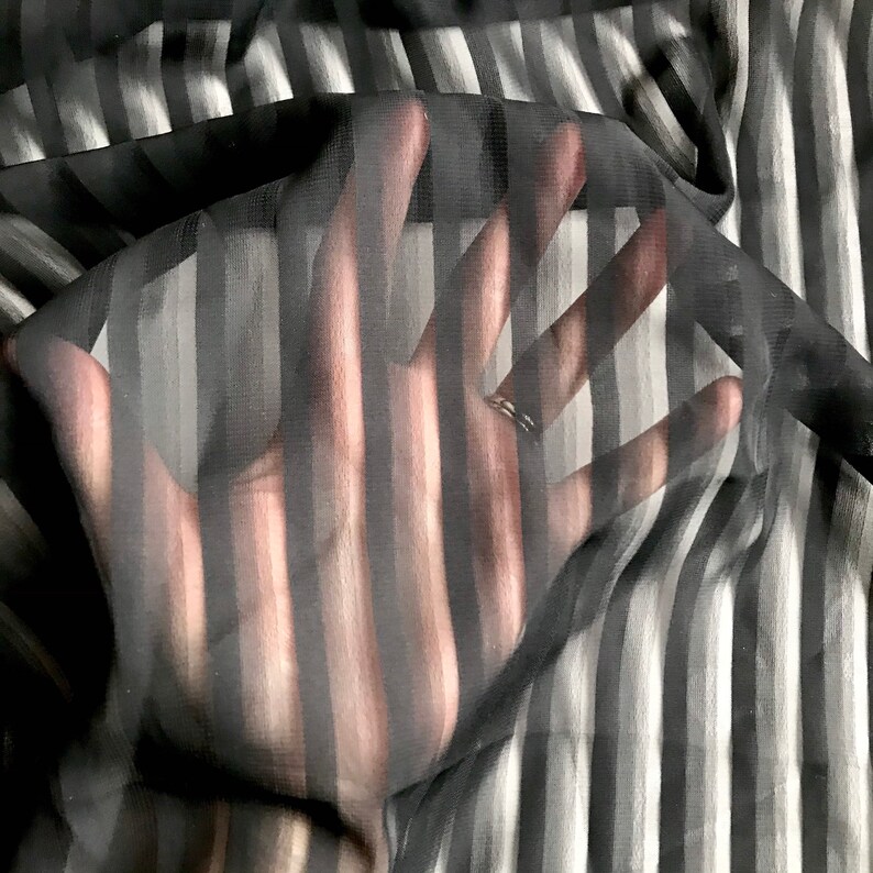 May include: Black and white striped sheer fabric with a hand reaching through it.