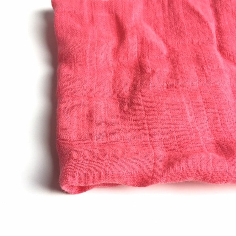 May include: A pink fabric swathe, folded and lying on a white surface. The fabric has a soft, textured appearance.