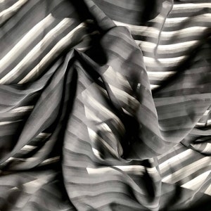 May include: Black sheer fabric with white stripes. The fabric is draped and folded, showing the texture and pattern.