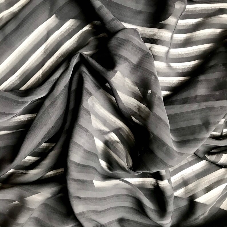 May include: Black sheer fabric with white stripes. The fabric is draped and folded, showing the texture and pattern.