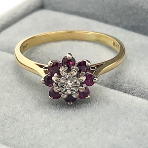 May include: A gold ring with a flower-shaped design featuring a cluster of red rubies and a single white diamond in the center.