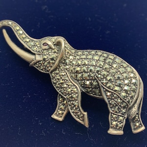 May include: A silver elephant brooch with a red stone eye, covered in sparkling marcasite stones.