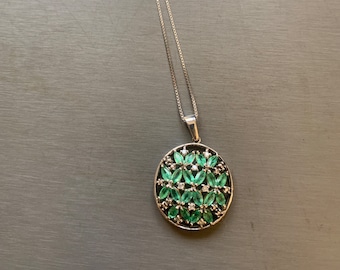 May include: A silver chain necklace with a round pendant featuring a cluster of emerald green and clear gemstones.