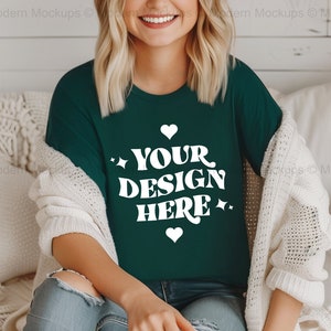May include: A woman wearing a dark green t-shirt with the text "YOUR DESIGN HERE" in white. The shirt has a distressed look and is worn with a white cardigan and blue jeans.