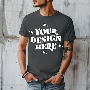 Può includere: Una maglietta grigia scura con una grafica bianca che dice "YOUR DESIGN HERE" con piccole stelle su entrambi i lati del testo.