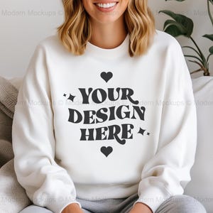 Pode incluir: Camisola branca com um gráfico preto que diz "YOUR DESIGN HERE" com corações de cada lado do texto.