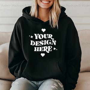 Pode incluir: Camisola de moletom com capuz preta com um gráfico branco que diz "YOUR DESIGN HERE" com corações e estrelas ao redor do texto.