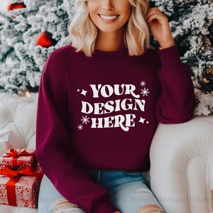 Peut inclure: Un sweat-shirt à manches longues de couleur bordeaux avec un col rond. Le sweat-shirt est imprimé à l'avant de flocons de neige blancs et du texte "YOUR DESIGN HERE".