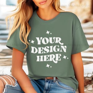 Puede incluir: Una camiseta verde salvia de manga corta y cuello redondo. La camiseta tiene el texto "YOUR DESIGN HERE" impreso en blanco en la parte delantera.