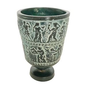 May include: A green ceramic cup with a black and white design of figures and a Greek inscription. The cup has a round base.