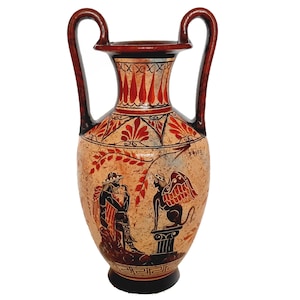 May include: A red and black Greek amphora with a white background. The amphora is decorated with a black and white image of a winged creature and a person holding a staff. The amphora has two handles and a narrow neck.