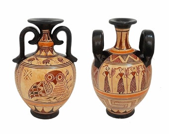 May include: Two ceramic Greek amphora vases with black handles and painted designs. One vase features an owl and the other features figures with wheat stalks.