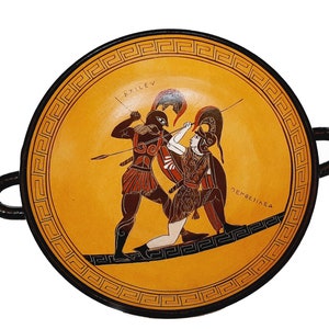 Könnte beinhalten: Eine schwarze und orangefarbene Keramikschale mit zwei Griffen. Die Schale zeigt eine bemalte Szene mit zwei kämpfenden griechischen Kriegern, mit dem Text "AXILLEV" und "NEPTESILEA" in griechischer Schrift.