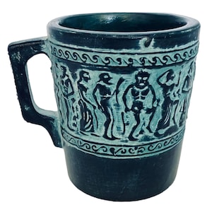 Puede incluir: Una taza de cerámica azul con asa, con un diseño en relieve de figuras de estilo griego. La taza tiene un esmalte azul oscuro y un diseño blanco.
