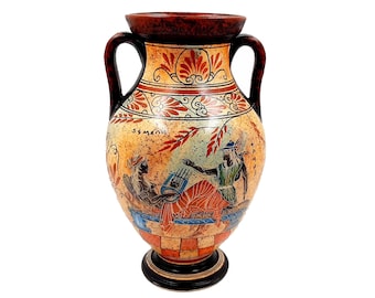 May include: A ceramic amphora vase with a red, white, and blue painted design. The vase features a scene of two figures playing music. The vase has two handles and a round base.