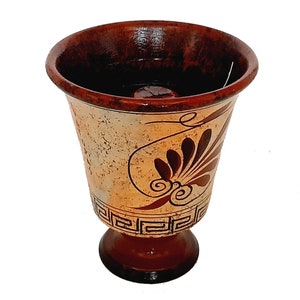 May include: A brown ceramic goblet with a white and brown geometric design. The goblet has a wide base and a narrow top.