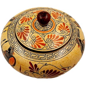 May include: A round ceramic container with a lid, decorated with a black and white geometric pattern and red and orange floral designs. The lid has a brown knob.