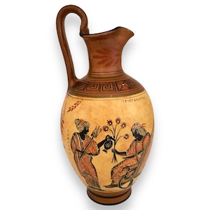 May include: A brown ceramic pitcher with a handle and a painted design of two figures in black, red, and white. The figures are holding flowers and a pitcher. The pitcher has a Greek inscription that reads "ΤΡΙΤΟΓΕΝΗΣ".