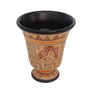 May include: A brown ceramic cup with a black rim and a base. The cup is decorated with a geometric pattern and an image of two owls in brown and orange.