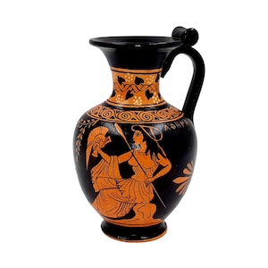 May include: Black and orange ceramic vase with a handle. The vase features a painted scene of figures in classical attire, with the word "ΛΘΗΝ" visible. The rim and handle are black, with orange accents and a floral design.