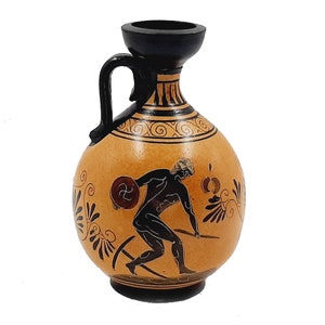 May include: A black and orange ceramic vase with a black handle and a black and white design of a figure holding a discus. The vase has a round body and a narrow neck.