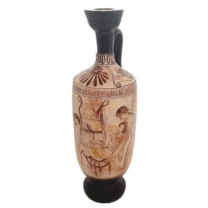 May include: A brown and black ceramic vase with a black handle and a geometric design. The vase is decorated with a scene of two figures in a reclining position.