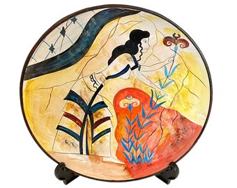 May include: A round ceramic plate with a painted design of a woman in a blue and yellow dress reaching for a flower. The background is a yellow and orange landscape with blue and green accents.