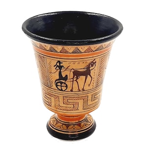 Pode incluir: Uma pequena taça de cerâmica laranja e preta com um design geométrico e um interior pintado de preto. A taça apresenta uma silhueta preta de uma carruagem puxada por um cavalo.