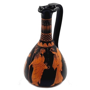 Puede incluir: Jarra de cerámica griega negra y naranja con asa y una escena de dos figuras pintadas en el lateral.