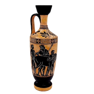 May include: A black and orange ceramic vase with a black and white design of figures and a horse. The vase has a narrow neck and a wide base.