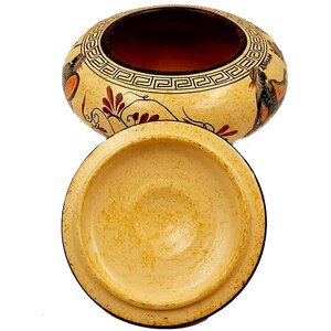 May include: A ceramic jar with a lid, decorated with a geometric pattern and floral motifs in red, orange, and black. The jar has a cream-coloured background and the lid is plain.