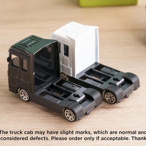 A toy model of a truck cab with two different color options, one black and one white, sitting on a wooden surface.