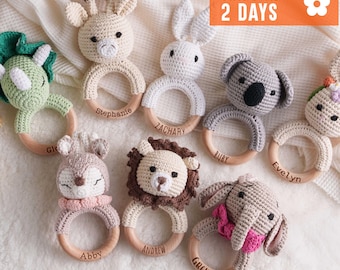 May include: A collection of seven crocheted animal rattles on wooden rings, including a green dinosaur, beige giraffe, white rabbit, gray koala, tan deer, brown lion, and gray elephant with a pink bow, each featuring a personalized name engraved.